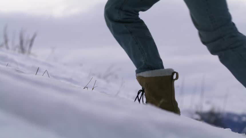 A person hikes up a snowy mountain slope on a cloudy day
