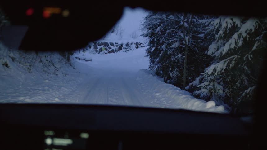 A vehicle with a windshield driving on a snowy road surrounded by trees