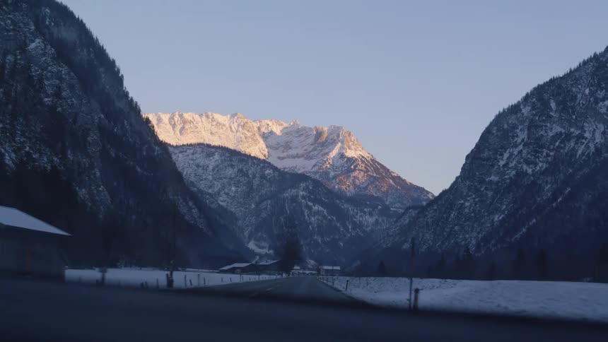 A vehicle travels down a road through a snow mountain valley on a clear day