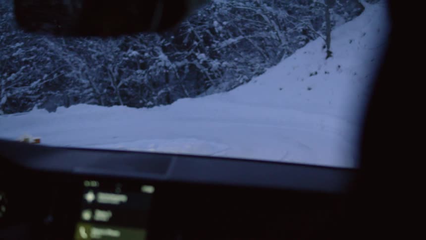 A person is driving a vehicle on a winding snowcovered road in a forested area