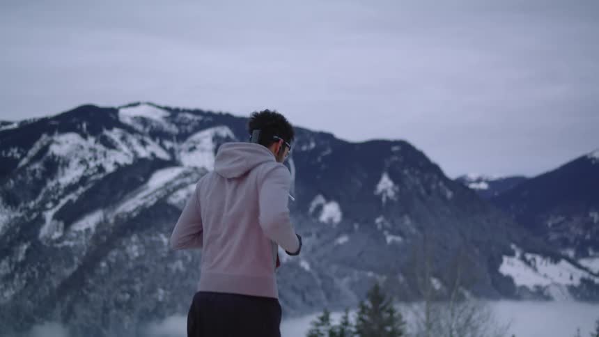 A man jogs on a snow covered road near mountains with ski trails