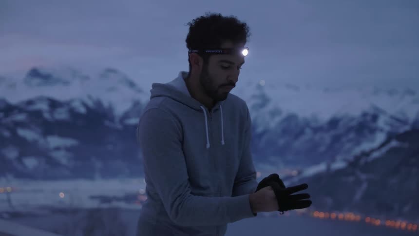 A man is standing outdoors putting a gloves on at dusk