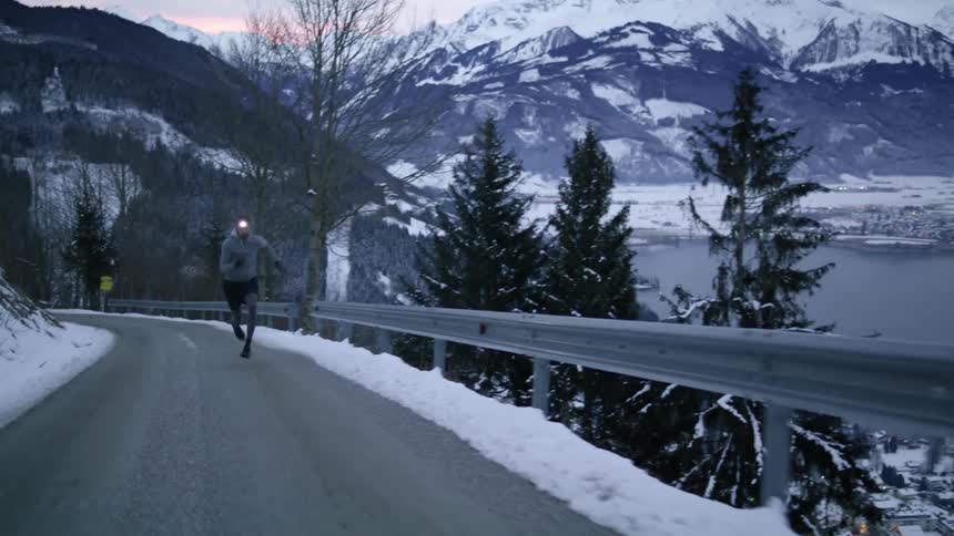 A man runs along a narrow road on a mountain slope at sunrise