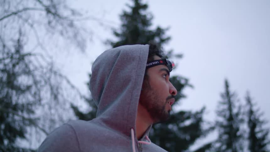 Fearful man wearing a hoodie and a headlamp looks around nervously in a forest