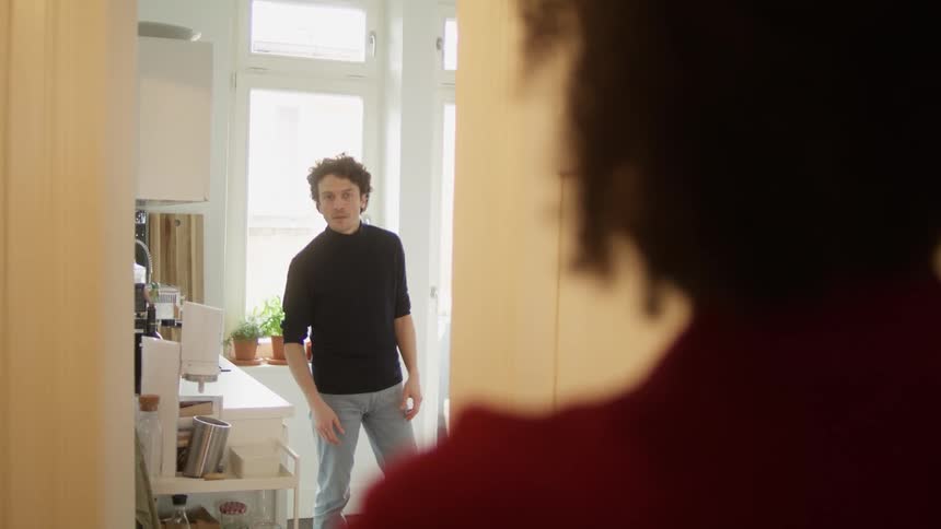 A man standing in a room at home yelling at someone and moving his hands around angrily at daytime