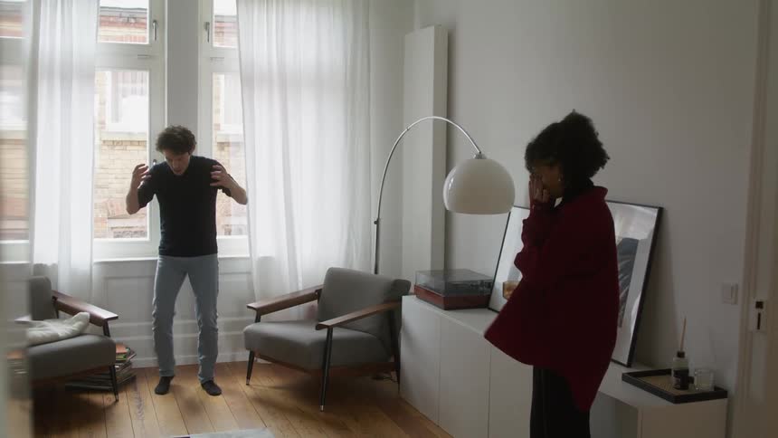 A woman covers her face in frustration while her husband screams and gestures during an argument