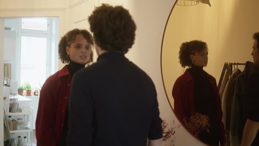 A man and a woman standing in a room next to a mirror arguing with a doorway in the background