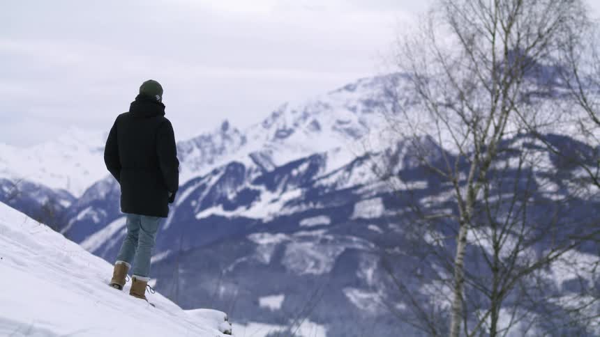 Man wearing a black parka climbing a snow covered slope near the mountains