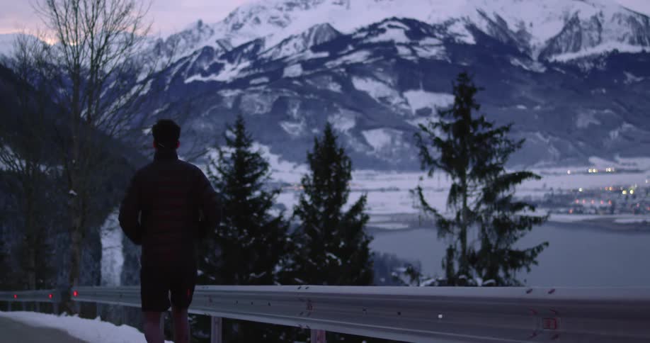 A man jogs on a snow covered road with a view of a mountain lake town