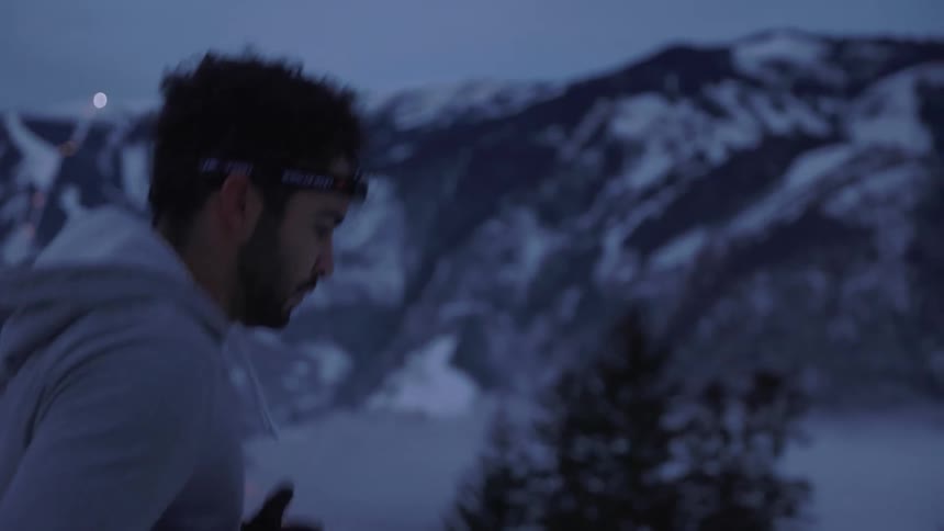 A man jogs through a snowy mountain range overlooking a town in the mountains valley in the evening