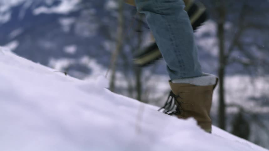 A person wearing boots climbing up a snow covered hill near the mountains