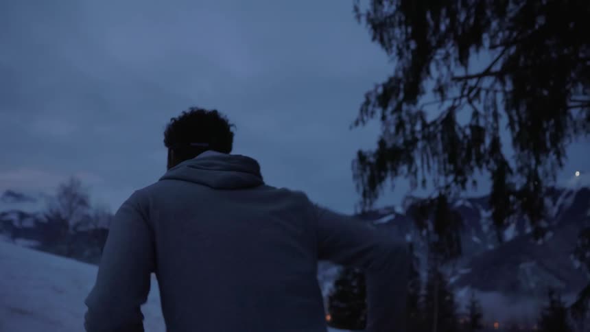 A man jogging in snowy mountains while wearing a headlamp in the dark
