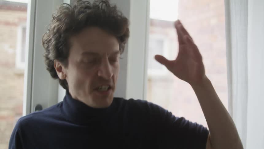 A man is yelling and using hand gestures while standing in front of a window