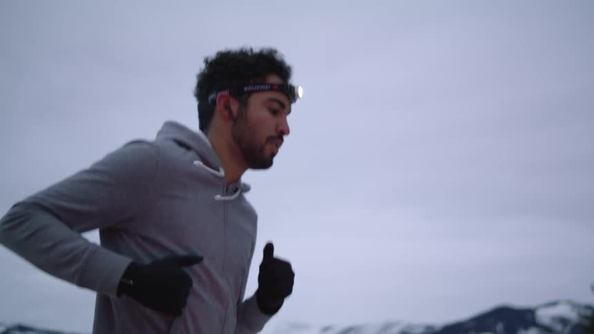 A man with a flashlight on his head jogging with trees the sky and clouds in the background
