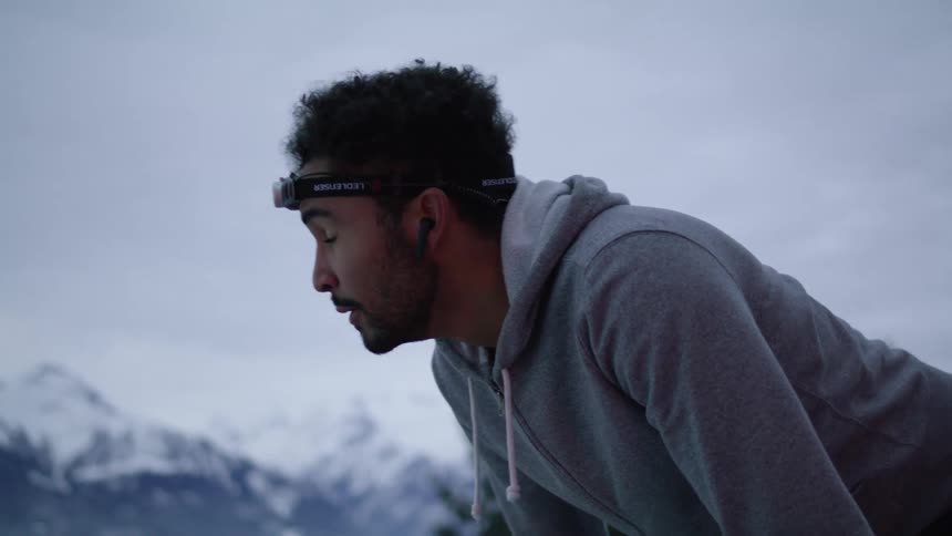 A man glances around at his surroundings while attempting to catch his breath outdoors in a mountainous area on a cloudy day