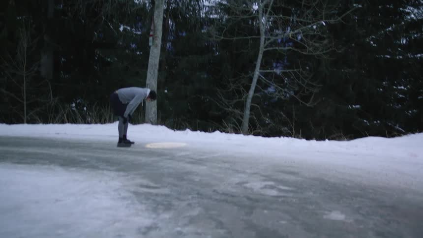 A man attempts to catch his breath while standing with his hands on his knees on an icy road