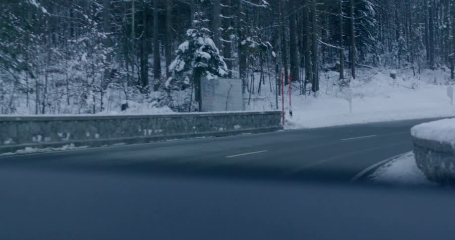 A vehicle with a windshield driving on a road surrounded by snow and trees