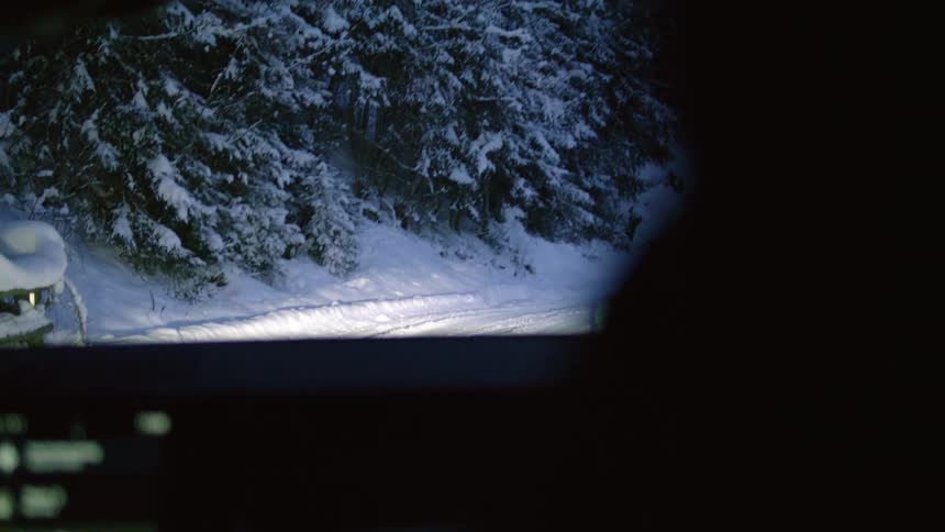 A vehicle travels down a narrow road covered in thick snow in the evening