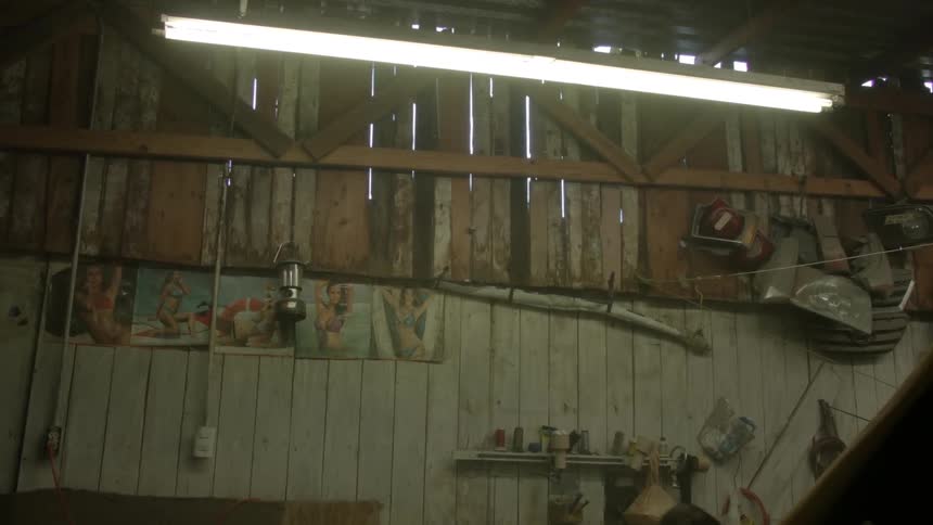A wooden wall of a shed has tools on the wall