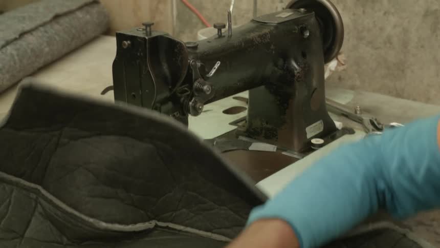 A person cuts some threat from fabric near a machine