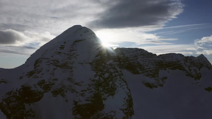 A mountain range covered in snow and ice with the sky and clouds in the background