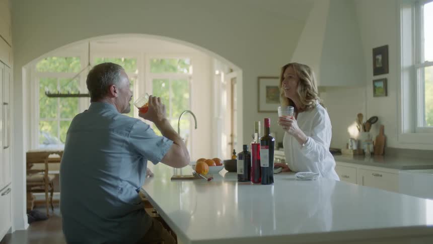 A man and woman make a toast with their glasses and then drink inside of a kitchen in a house at daytime