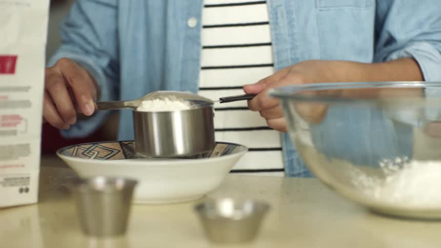 A person with a knife shaping cooking flour in a cylinder over a bowl on a counter