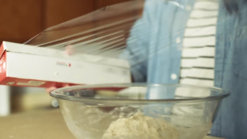 A person is wrapping a bowl of food with plastic