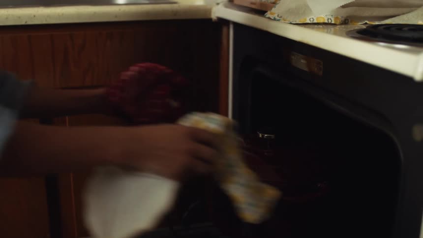 A woman moves a roasting pan from on top of the stove to an oven rack in a home kitchen