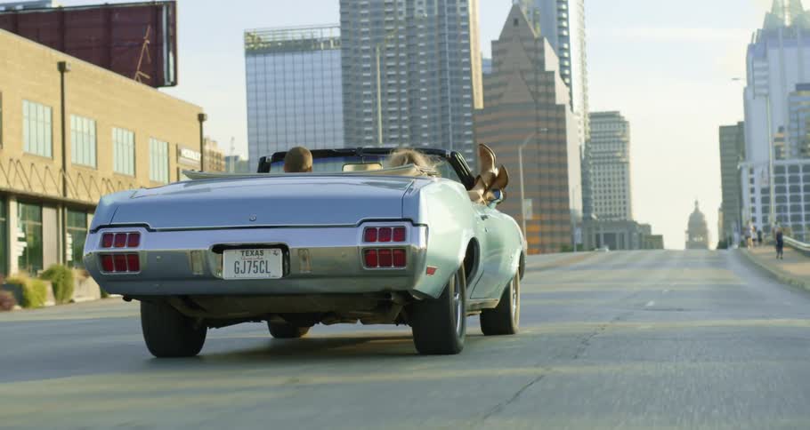 Woman with her feet hanging out a convertible car driving on the highway through the city atmorning