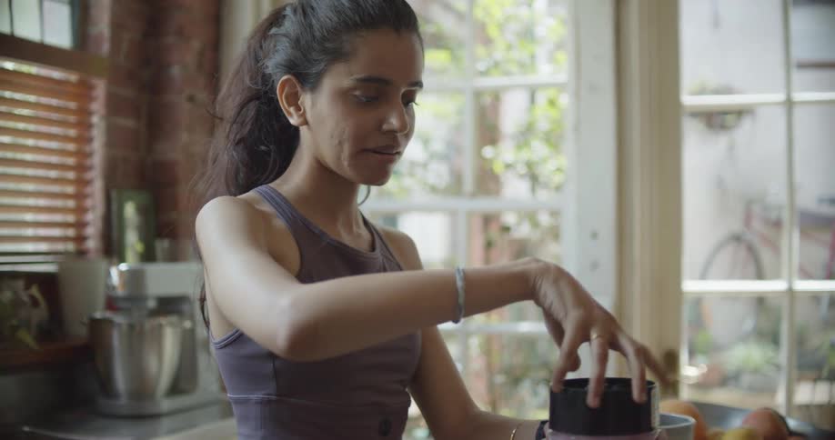 A woman in a sports bra making a smoothie at home