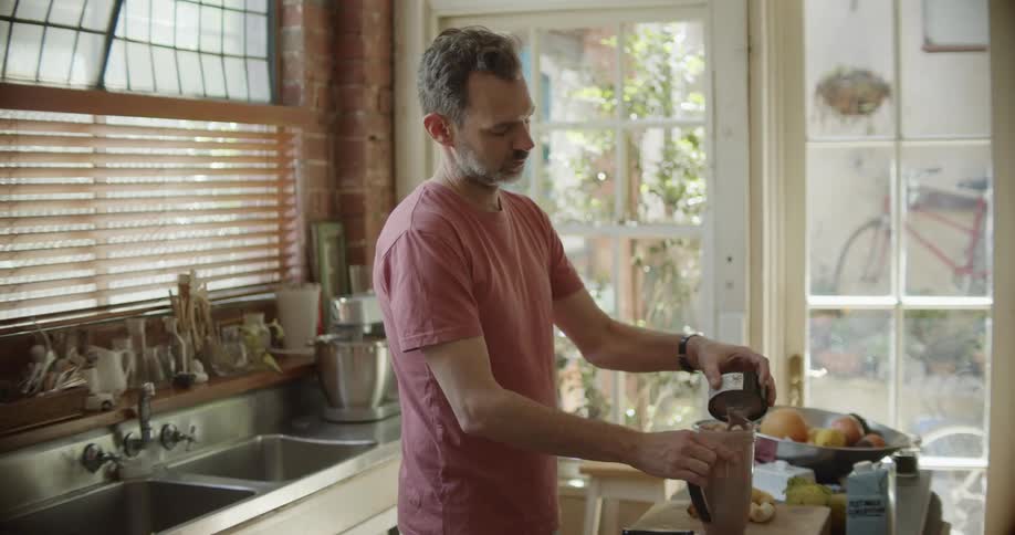 A man making a fruit smoothie in a blender at home