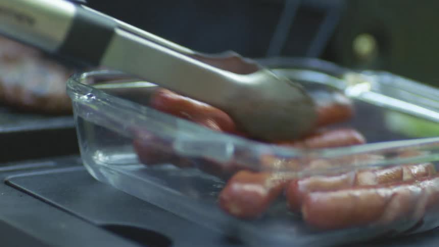 Freshly cooked sausages steaming on a glass bowl near a barbeque