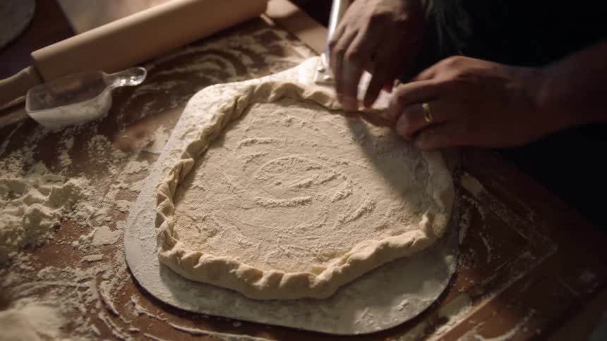 A person folding the edgees of a home made pizza over the kitchen counter top at home