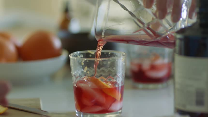 A person in a room pouring a drink into a glass on a table