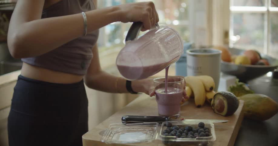 A woman in the kitchen pouring a smoothie into a glass on the counter