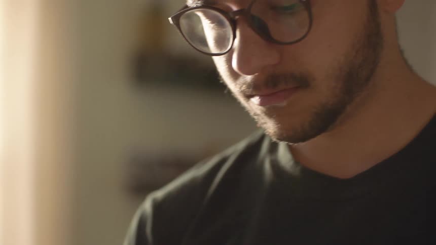 Young bearded man wearing glasses near a window in a room at home