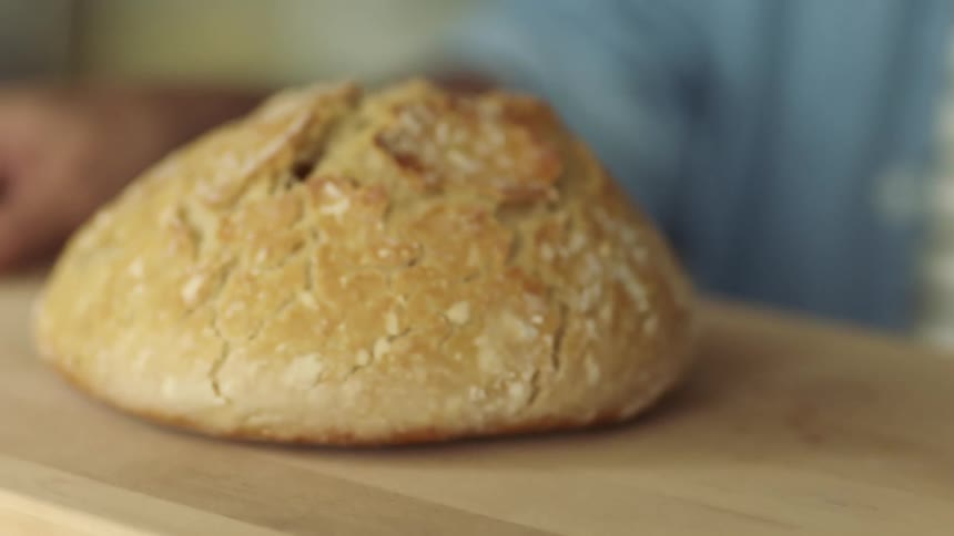 A person carries a cutting board with baked bread atop and places it on a kitchen counter