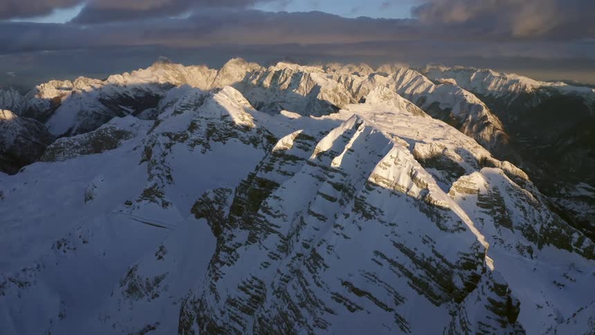 A mountain range covered in snow and ice with the sky and clouds in the background