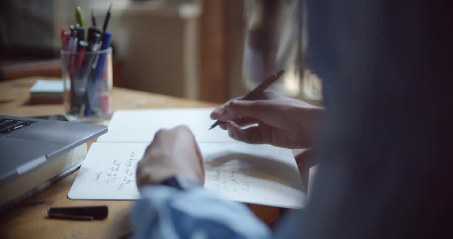 A woman holds a pen in her hand and writes in a notebook on a table in a living room
