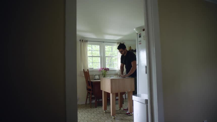 A man in the kitchen kneading dough with a wall and a window in the background