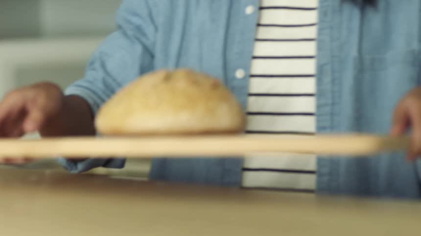 A woman carries a piece of bread on a cutting board to a counter
