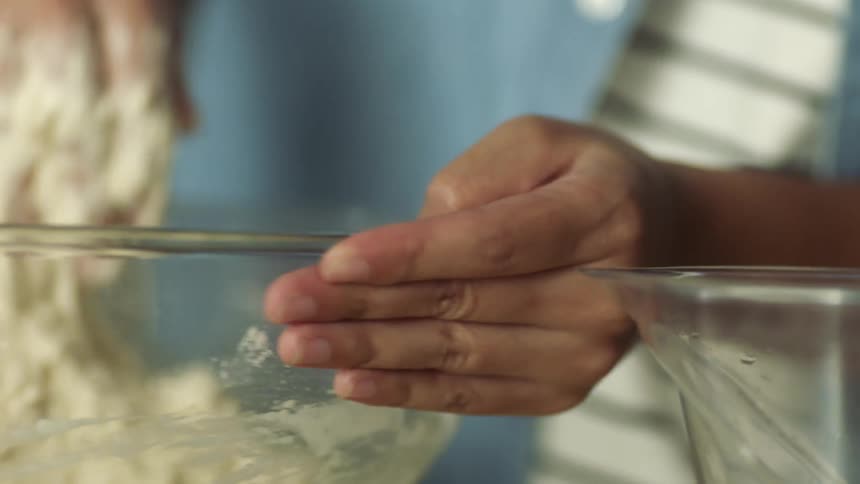 A person mixes and kneads dough in a glass bowl