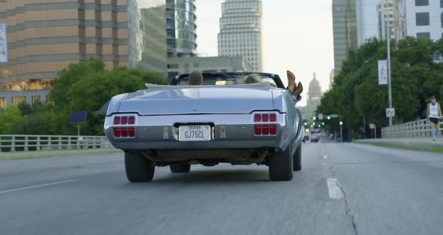 Woman with her feet hanging out a convertible car driving on the highway through the city atmorning
