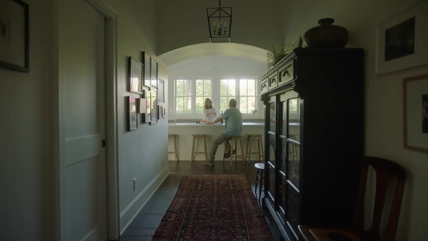 A man and a woman in a room with the man sitting on a stool next to a counter