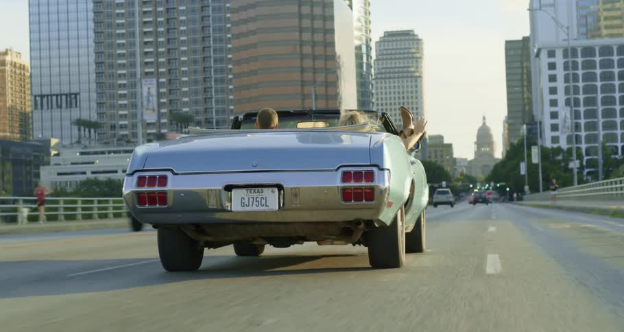 Woman with her feet hanging out a convertible car driving on the highway through the city at morning