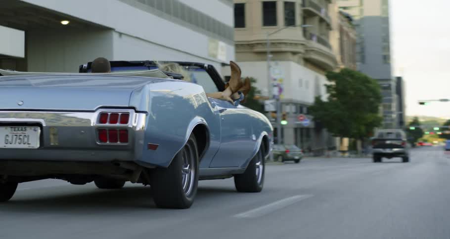 Woman with her feet hanging out a convertible car driving on the highway through the city atmorning