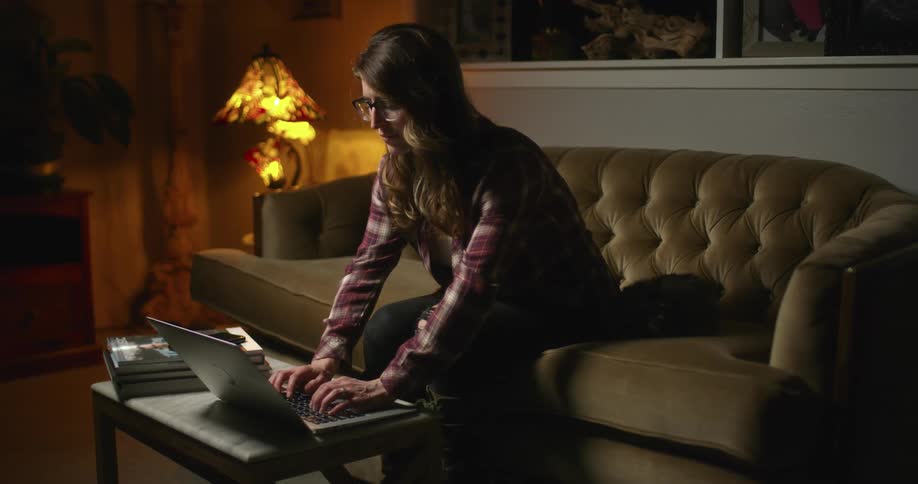 A woman pauses typing on her laptop to push her long hair back behind her ear