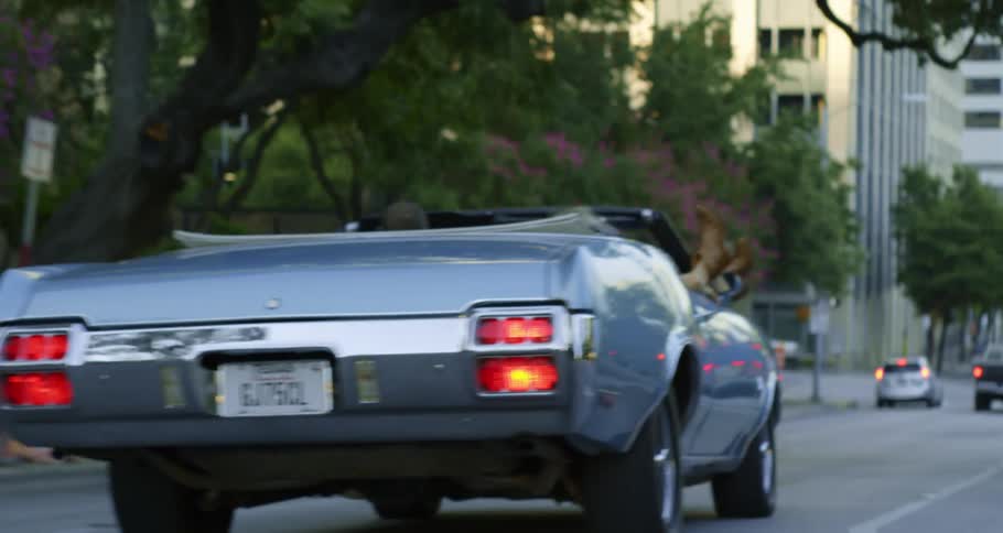 A woman props her feet out of a silver convertible while a man drives down a street at daytime