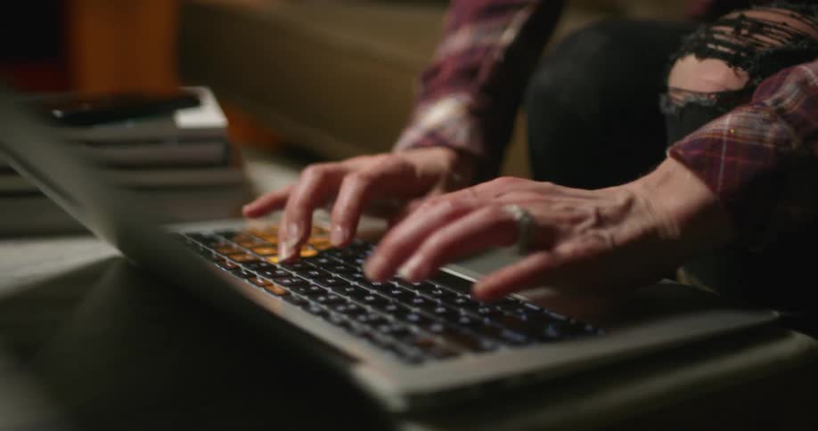 A person typing on the keyboard of a laptop over a coffee table in the living room